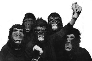 Black and white photo of guerilla girls art group. 5 women dressed in guerrilla masks. One with fist raised in defiance and resistance